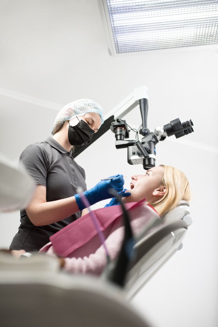 Dentist using a microscope for precise examination in a modern clinic setting.